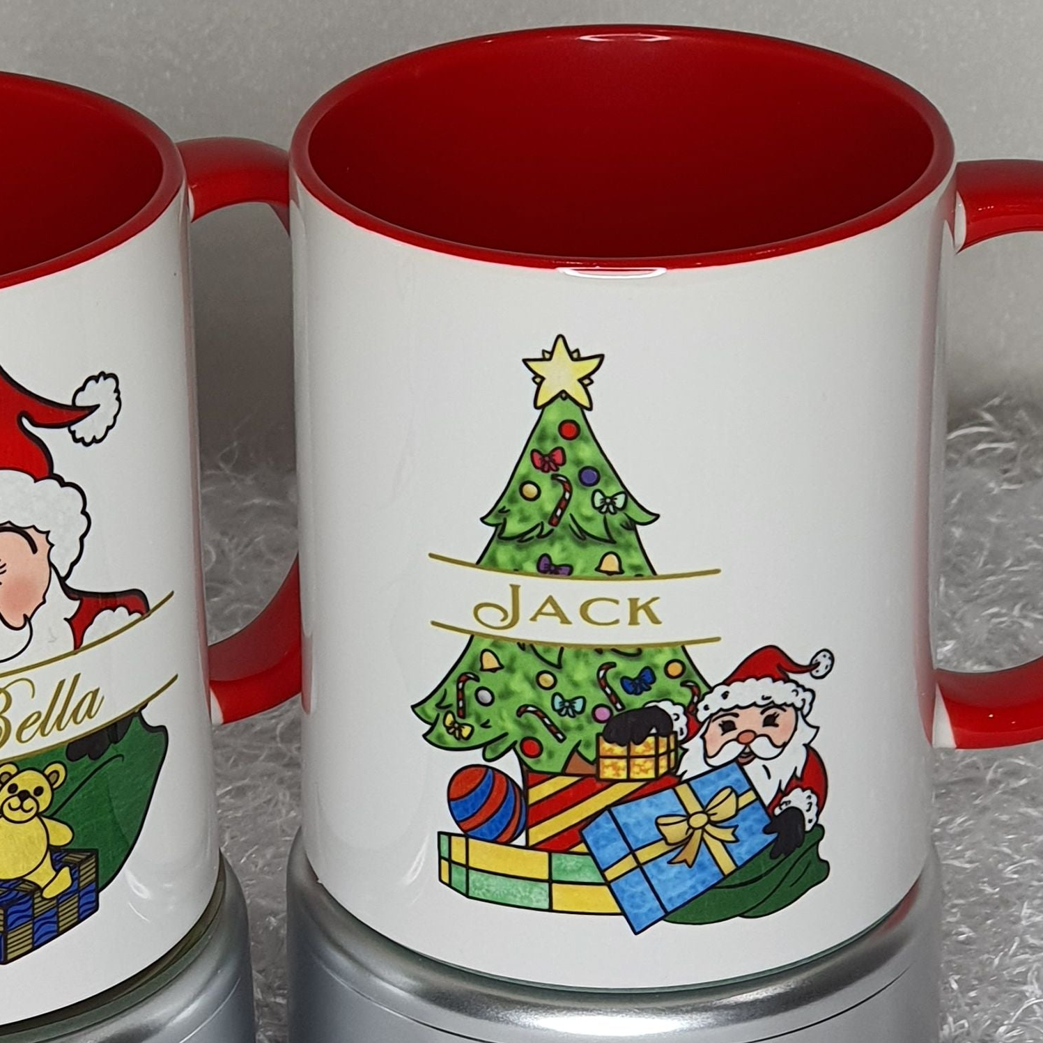 Two Christmas-themed mugs with Santa Claus and a tree design on a gray surface.